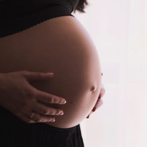 pregnant woman in black top holding bare belly
