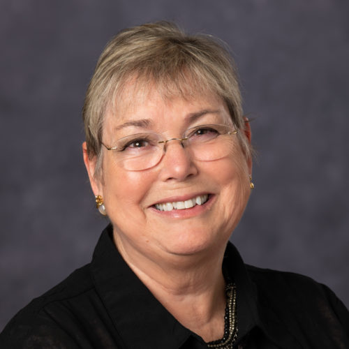 headshot of woman with short hair, glasses, and black top