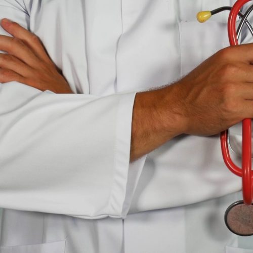 person in white lab coat holding red stethoscope