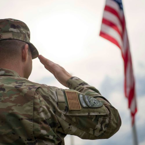 soldier in camouflage saluting American flag
