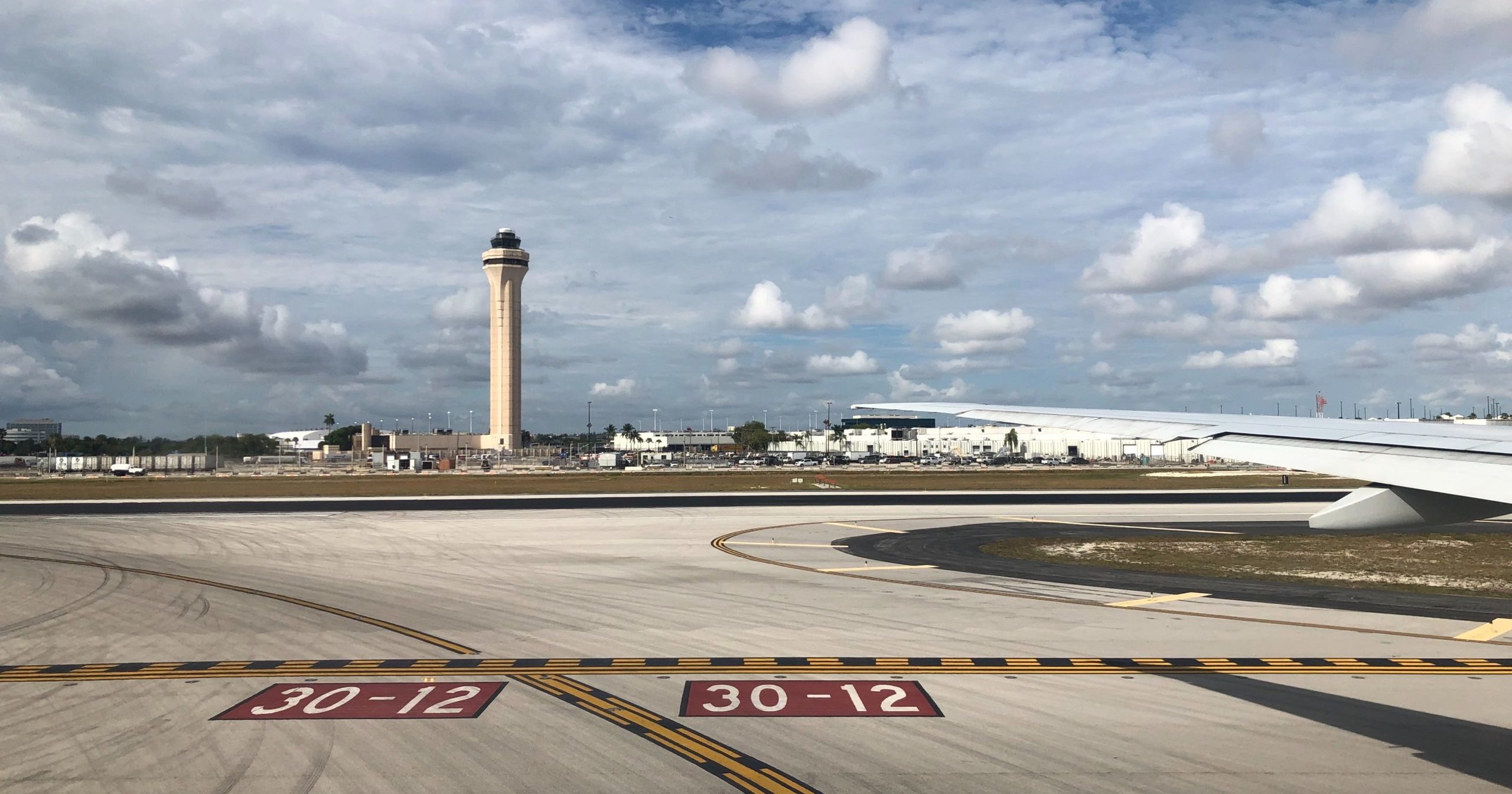 airport runway with tower in background and puffy white clouds in sky