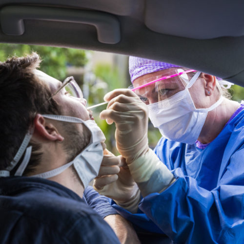 Masked doctor taking nasal swab of man in car