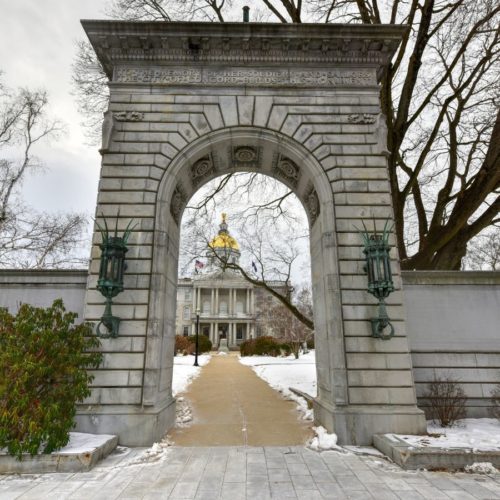 A photo of the New Hampshire State House through a stone gateway.